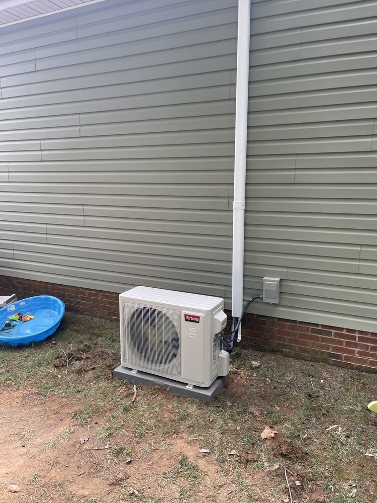 A white air conditioner is sitting on the side of a house next to a pool.