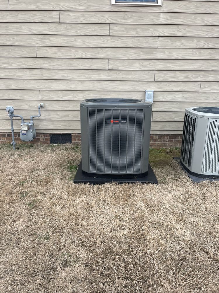Two air conditioners are sitting in the grass in front of a house.
