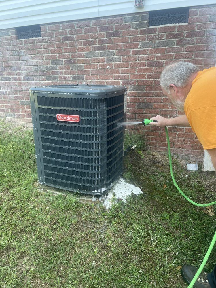 A man is cleaning an air conditioner with a hose.