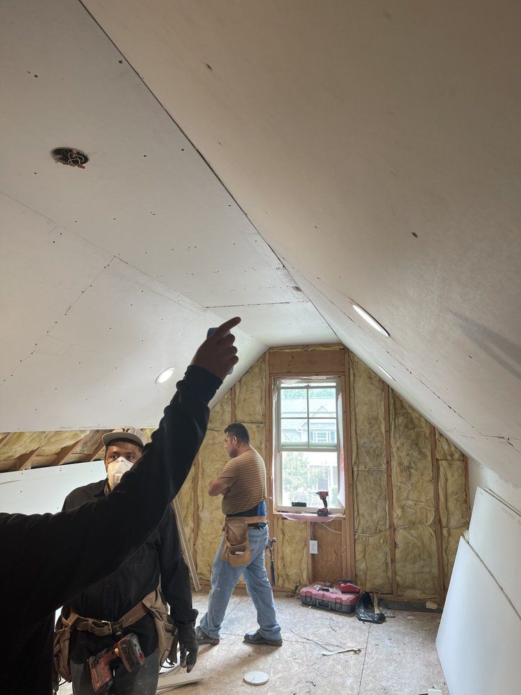 Two men are working on a ceiling in an attic.