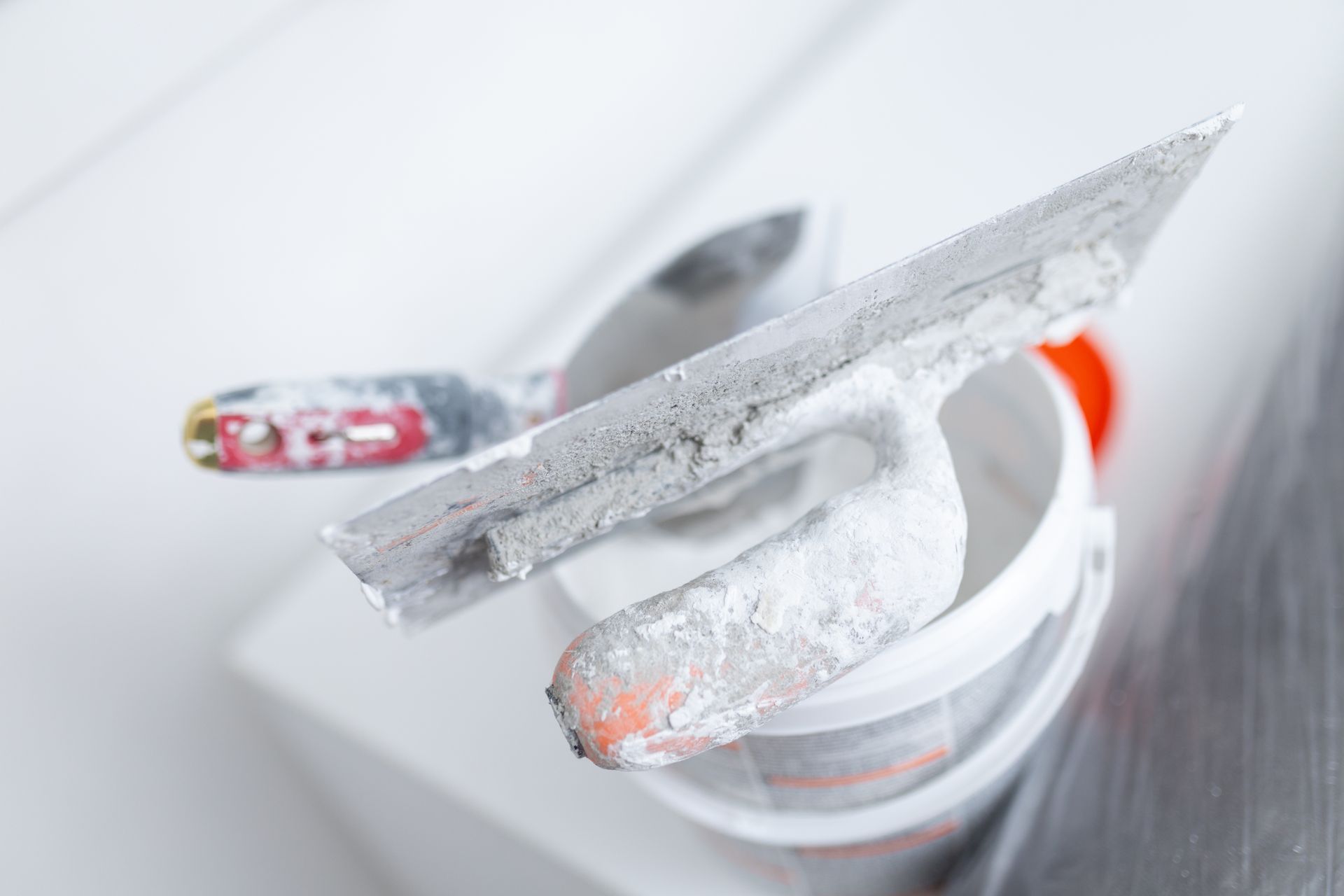 A close-up of plastering tools with wall putty on a bucket during a renovation.
