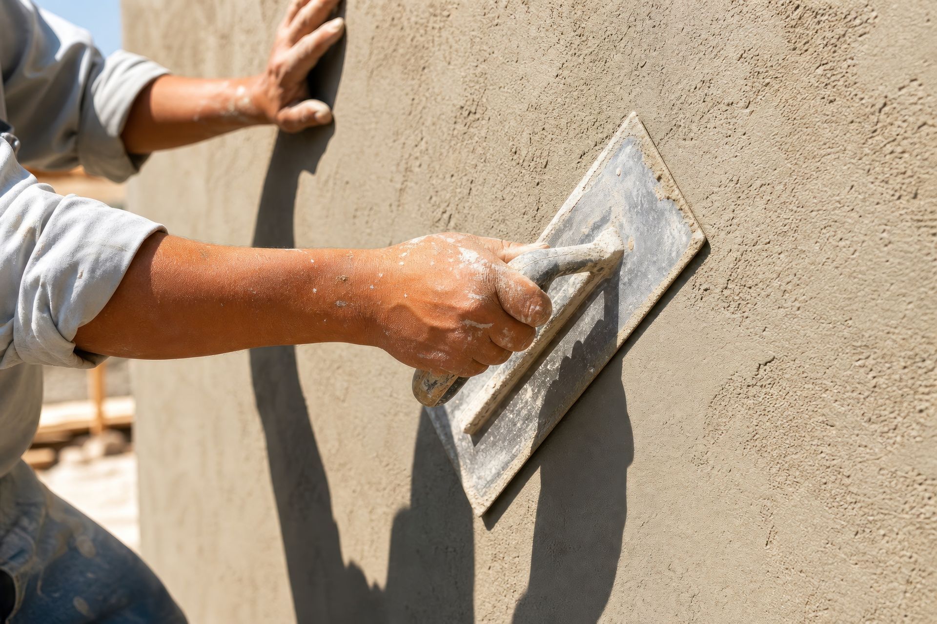 Professional builder applying wet plaster to concrete wall with metal trowel