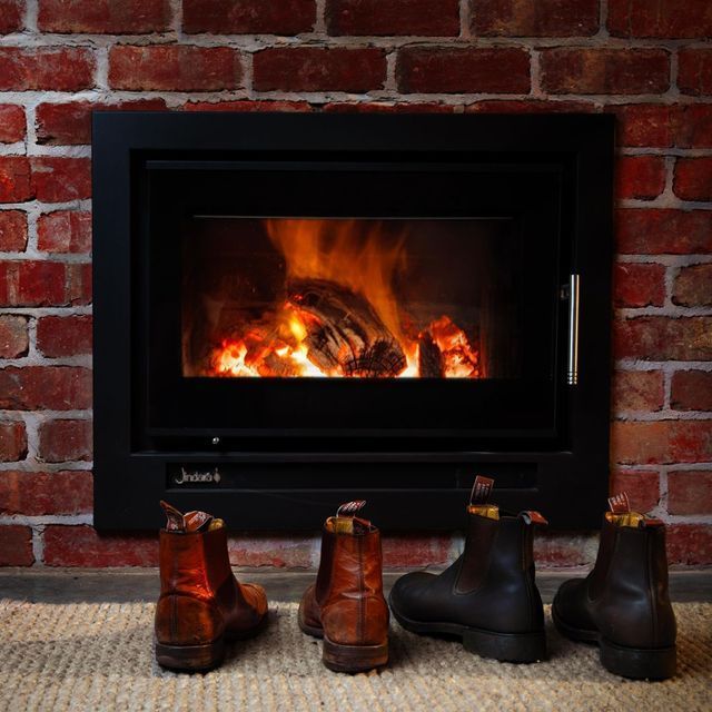 Three boots are lined up in front of a fireplace