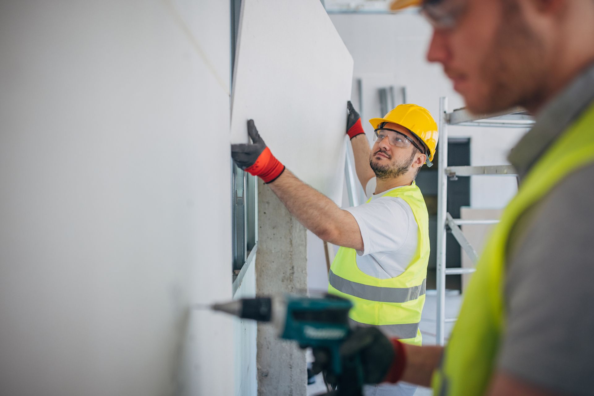 Two men in safety vests working on a wall, showcasing plastering supplies.