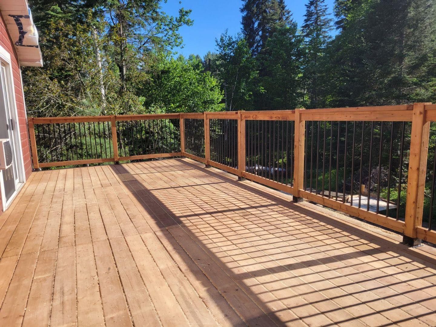 Une terrasse en bois avec une balustrade en métal et des arbres en arrière-plan