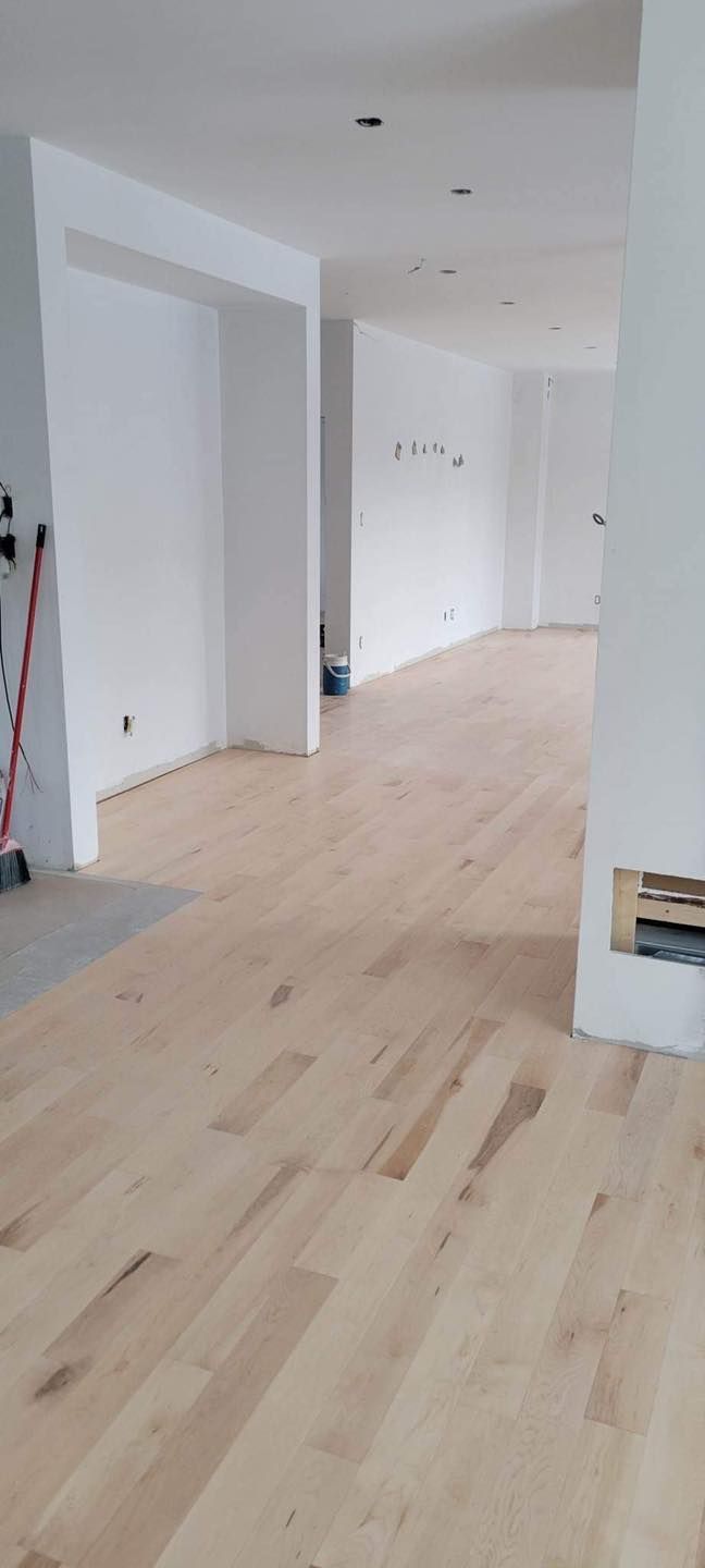 Une grande pièce vide avec un plancher en bois et des murs blancs.