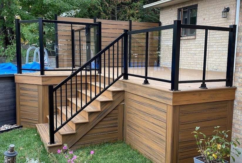 Une terrasse en bois avec des escaliers et une rampe en métal devant une maison.