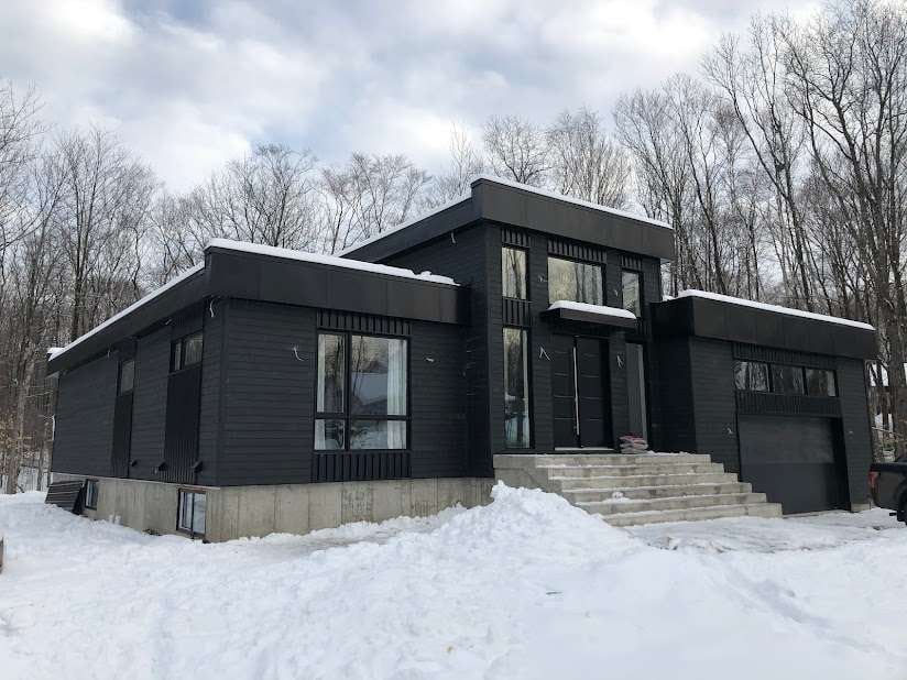 Une maison noire est assise au milieu d'un champ couvert de neige.
