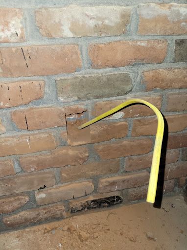 A yellow pipe is sticking out of a hole in a brick wall.