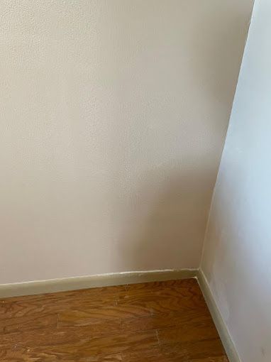 A corner of a room with a white wall and wooden floor.