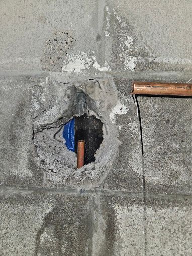A hole in a concrete wall with a copper pipe coming out of it.