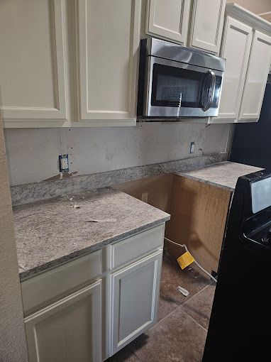 A kitchen with white cabinets , granite counter tops , stainless steel appliances and a black refrigerator.