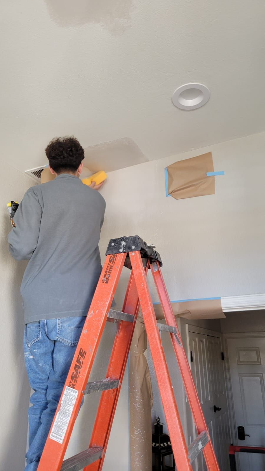 A man is standing on a ladder working on a wall.