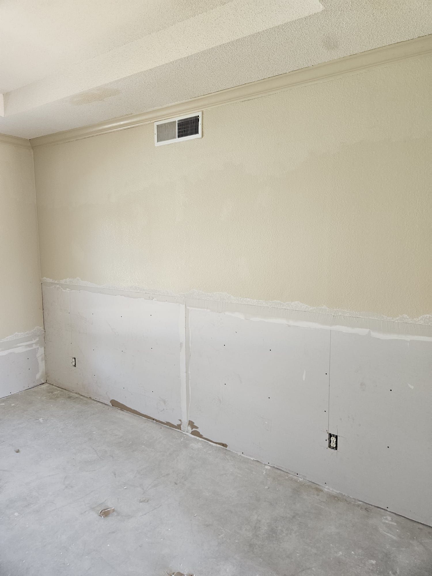 An empty room with a white wall and a concrete floor.