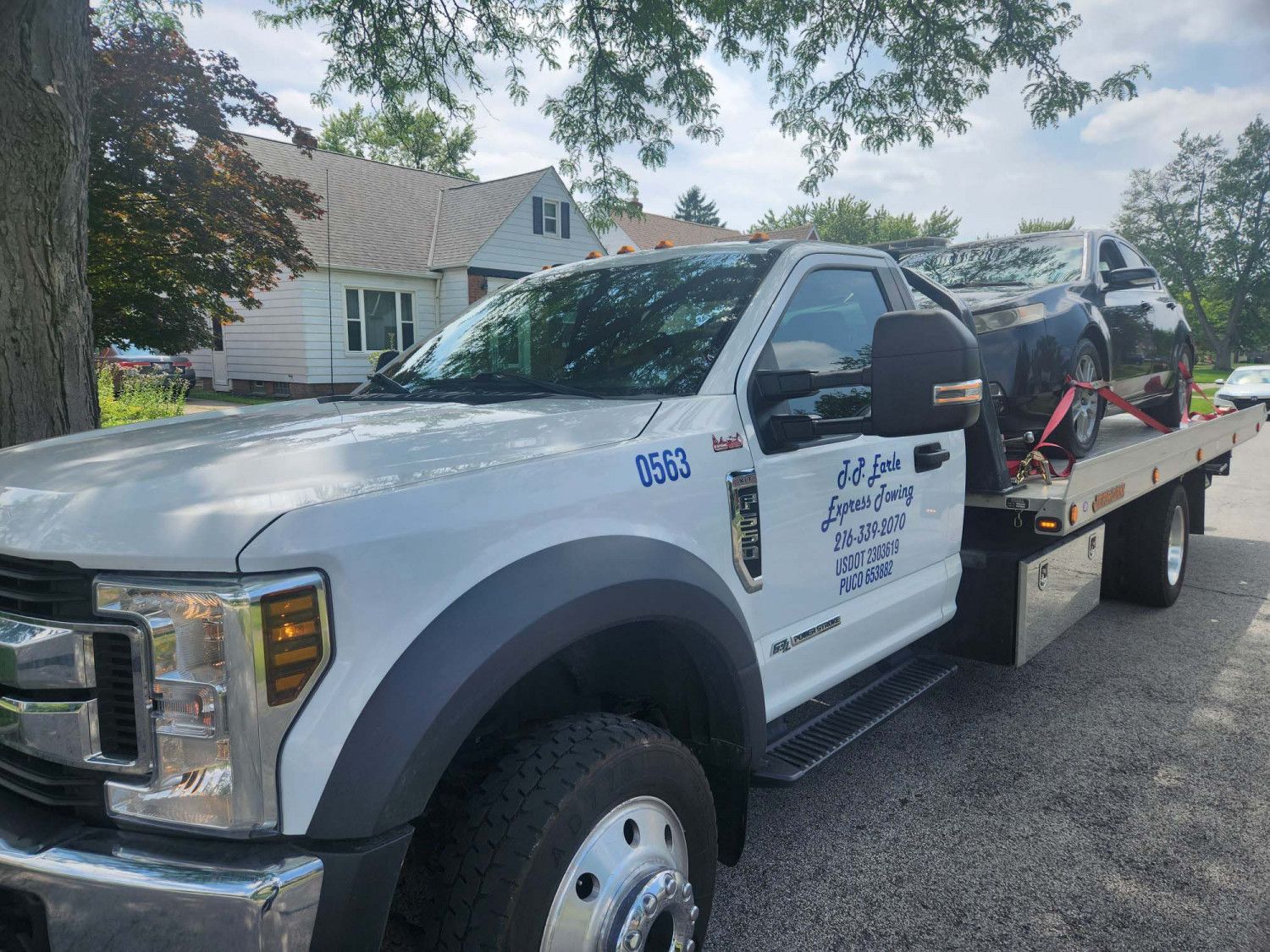 White tow truck carrying a black car. Truck parked on a residential street.