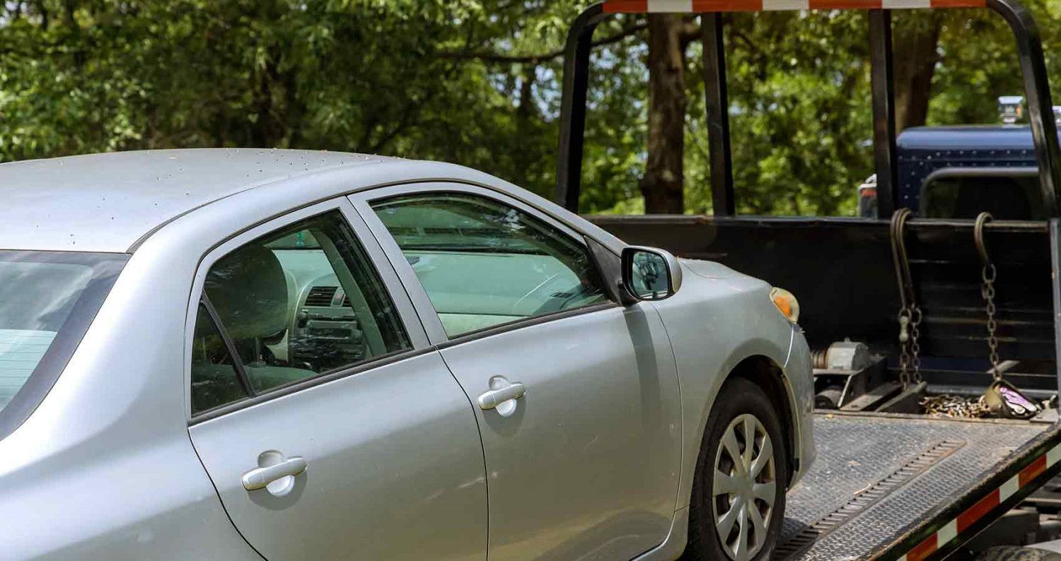 Silver car being towed on a flatbed tow truck outdoors.