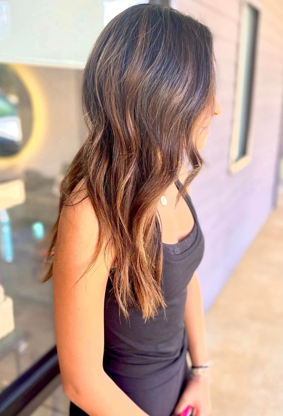 Woman with long, wavy brown hair and a black tank top stands outdoors, looking to the right.