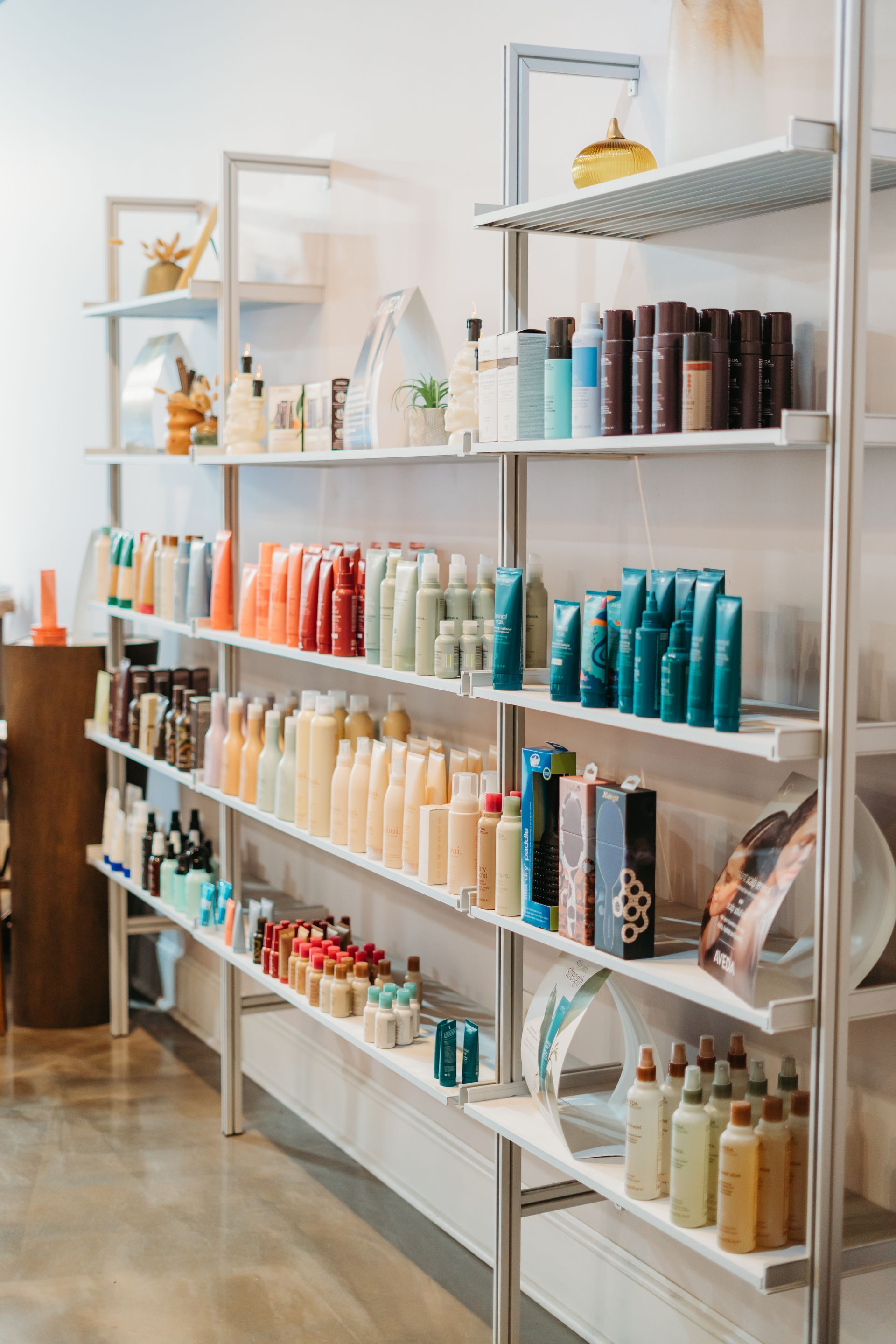Shelves in a beauty salon stocked with various colorful hair care products. White shelving against a white wall.