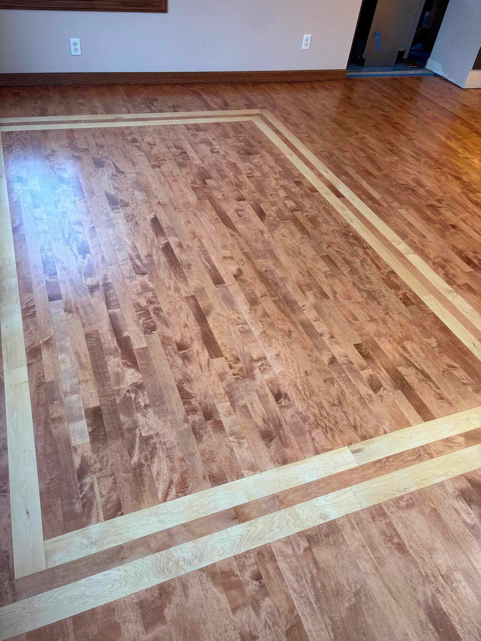 Image of multicolour hardwood floor.   You can see a light brown hardwood floor with a lighter square outline of hardwood planks. 