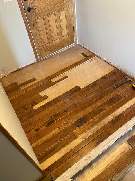 Image of a hardwood floor that is getting installed. You can see the entryway of a home with a wooden door and hardwood floor planks getting installed. 