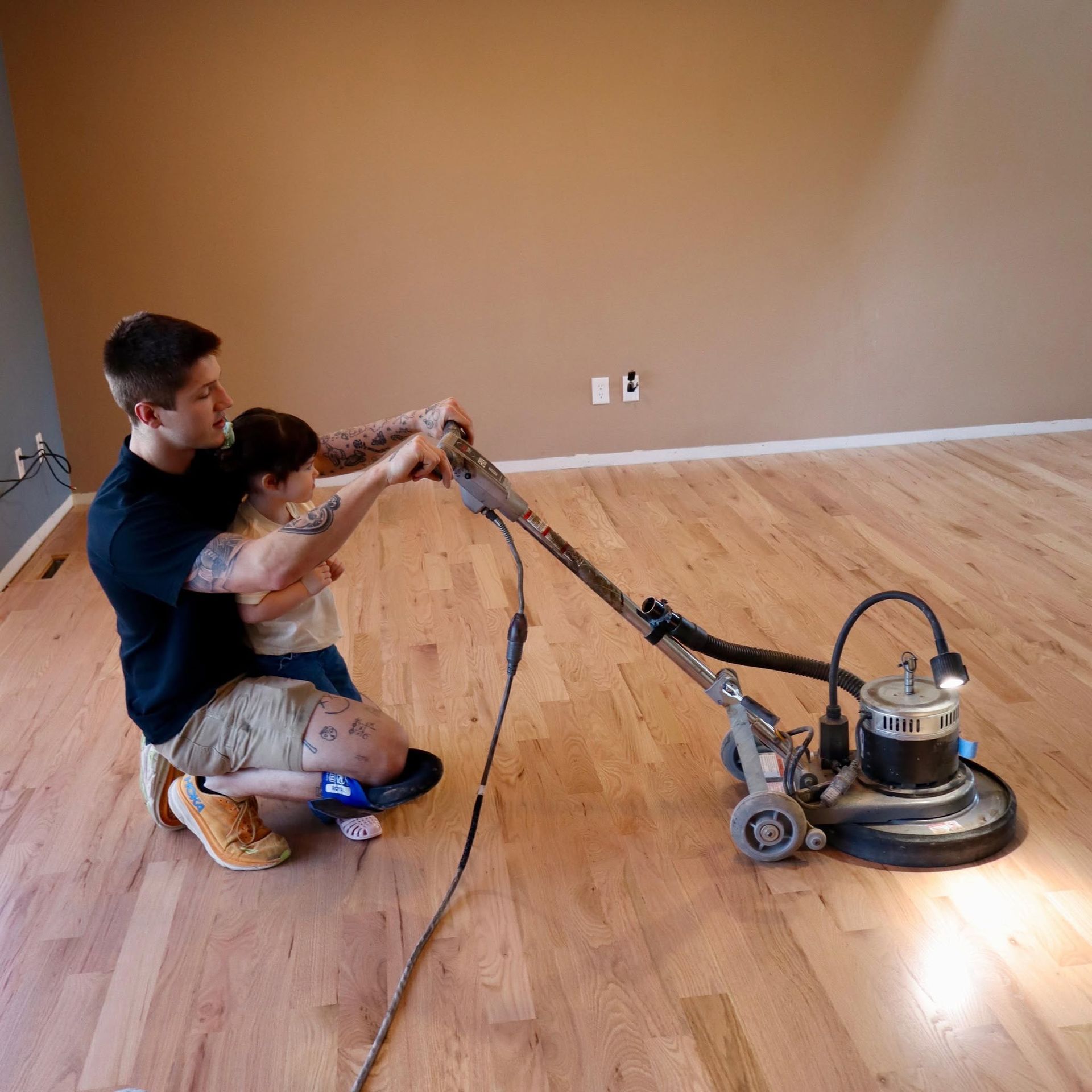 Image of Rylee owner of InfinityFlooring showing how to refinish a hardwood floor. You can see Rylee using a floor refinishing machine to polish a hardwood floor.