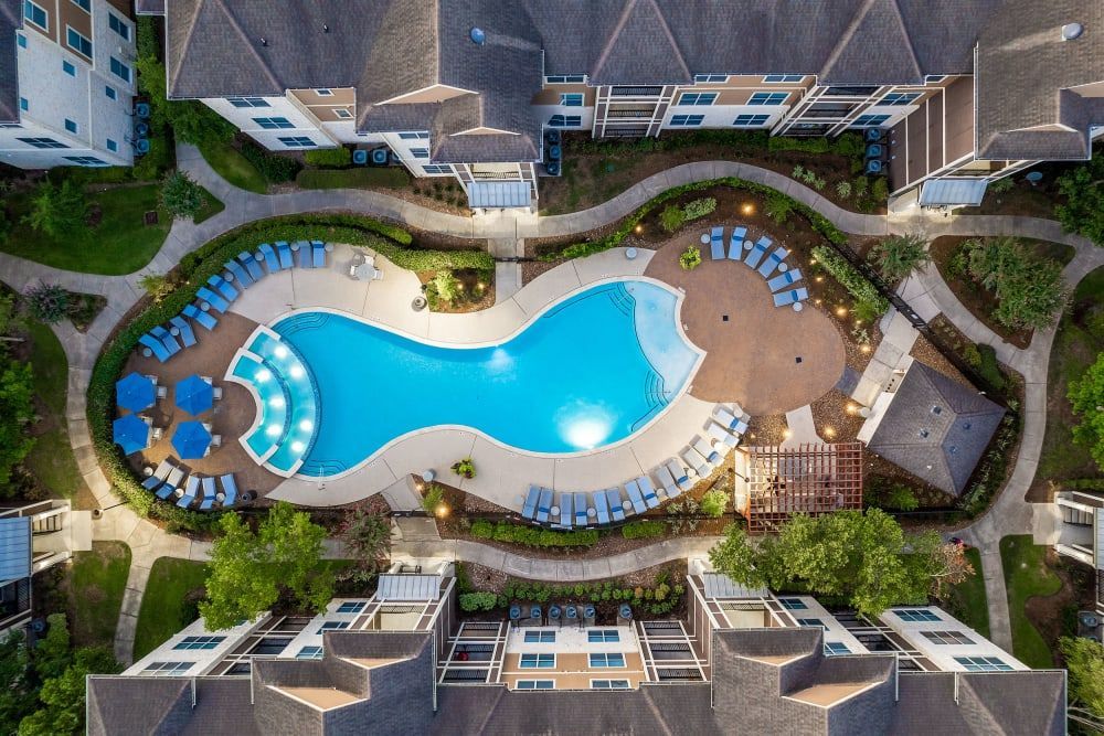 An aerial view of a large swimming pool surrounded by apartment buildings at Marquis at The Woodlands in Spring, TX.