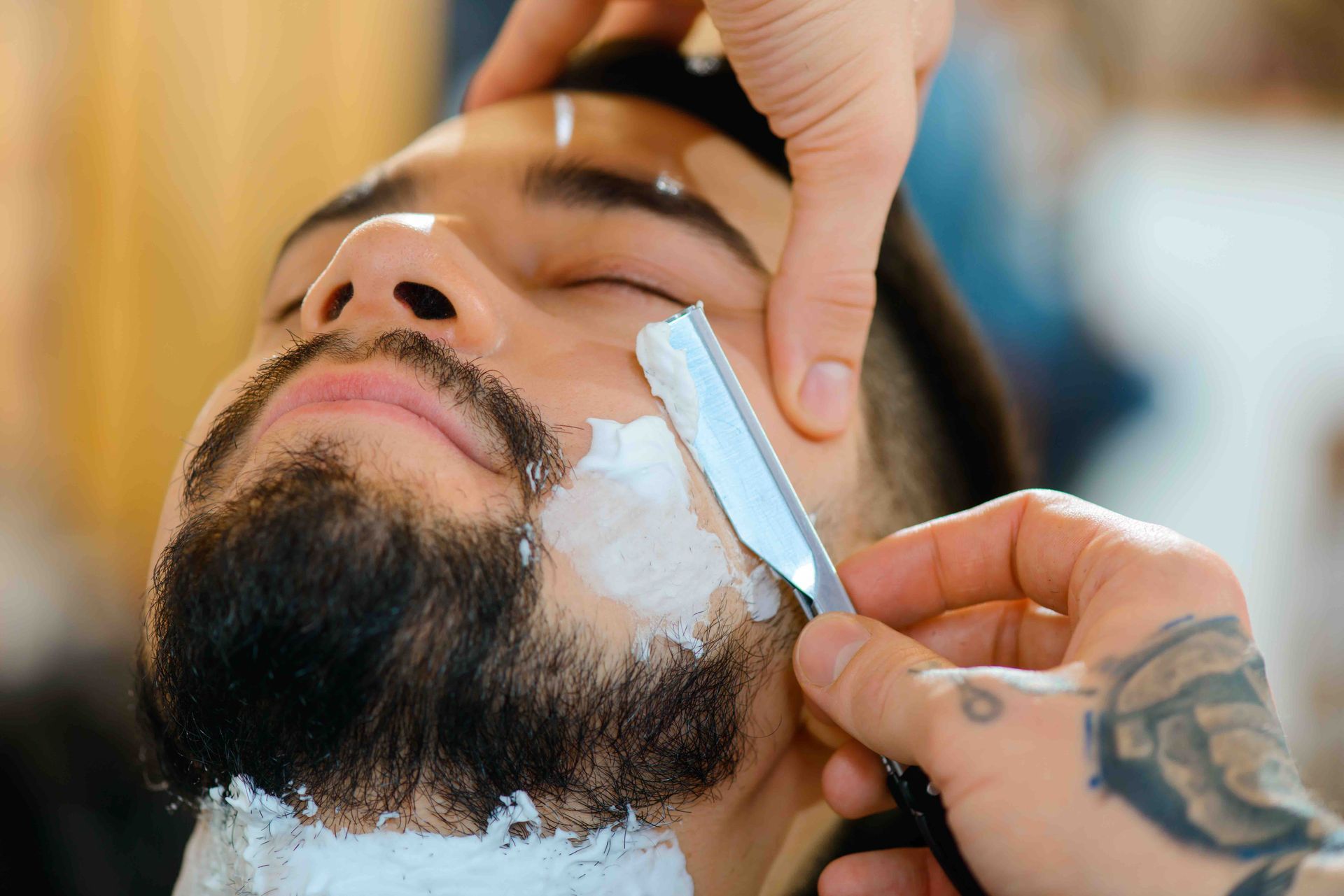 A man is getting his beard shaved by a barber with a razor.