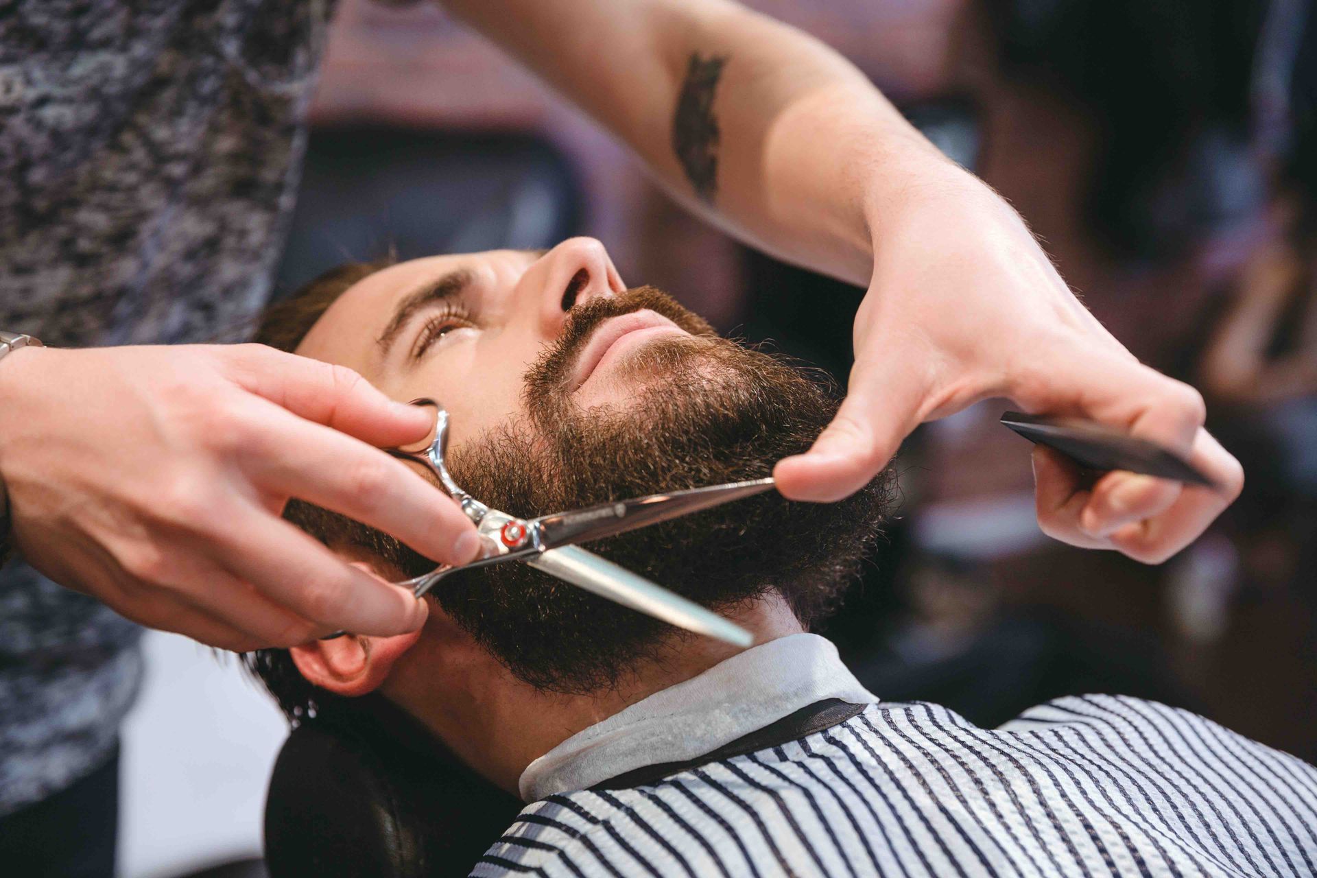 A man is getting his beard cut by a barber with scissors.