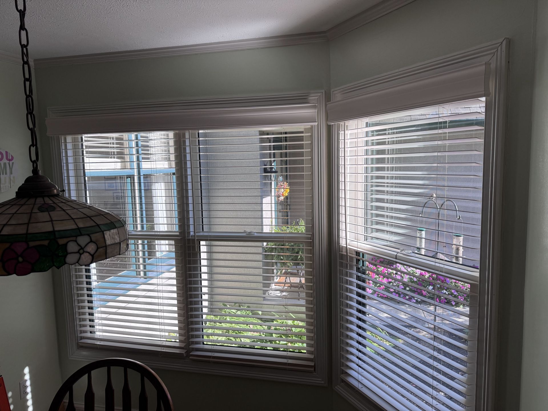 Bay window with white blinds, view of outdoors, and a decorative lampshade.