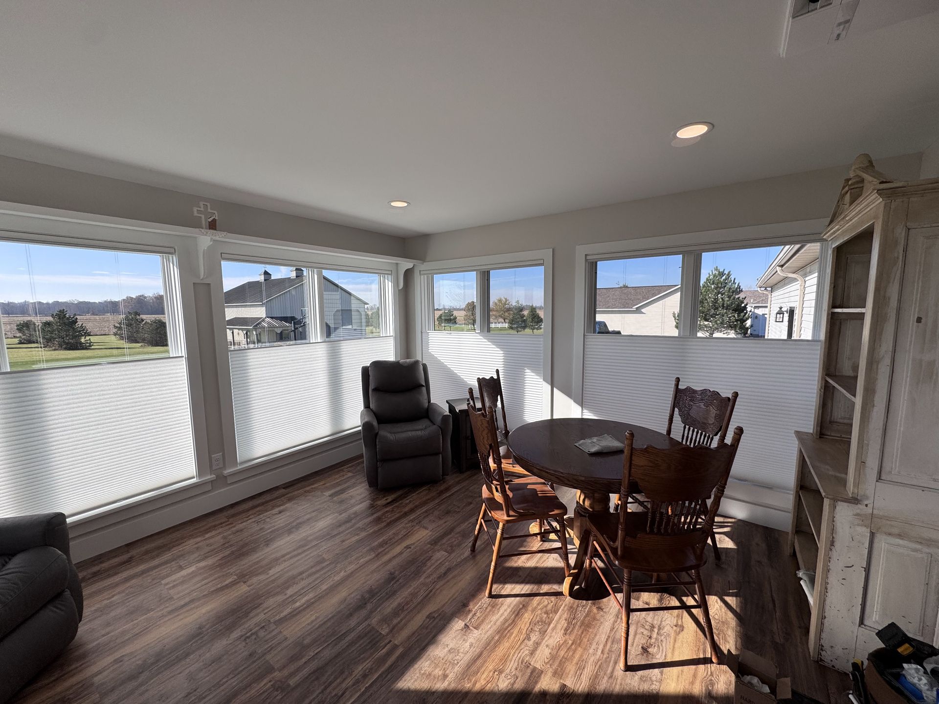 Sunroom with table, chairs, recliner, and a cabinet. Windows with blinds and wood floor.