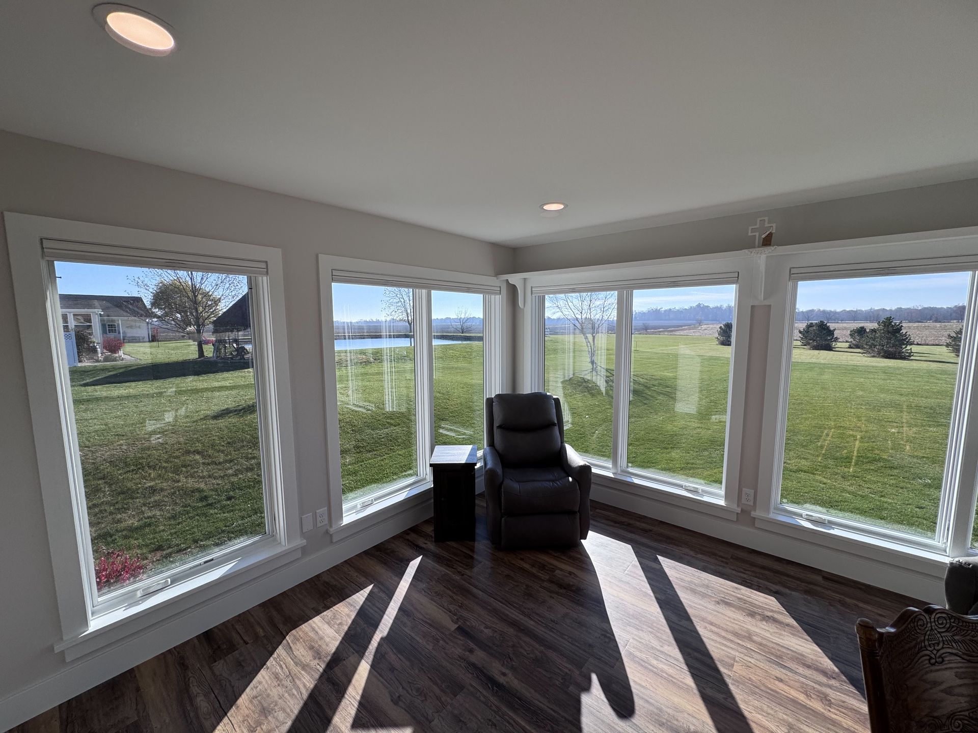 Sunroom with large windows overlooking a green field, recliner, small table, and wood-look floor.