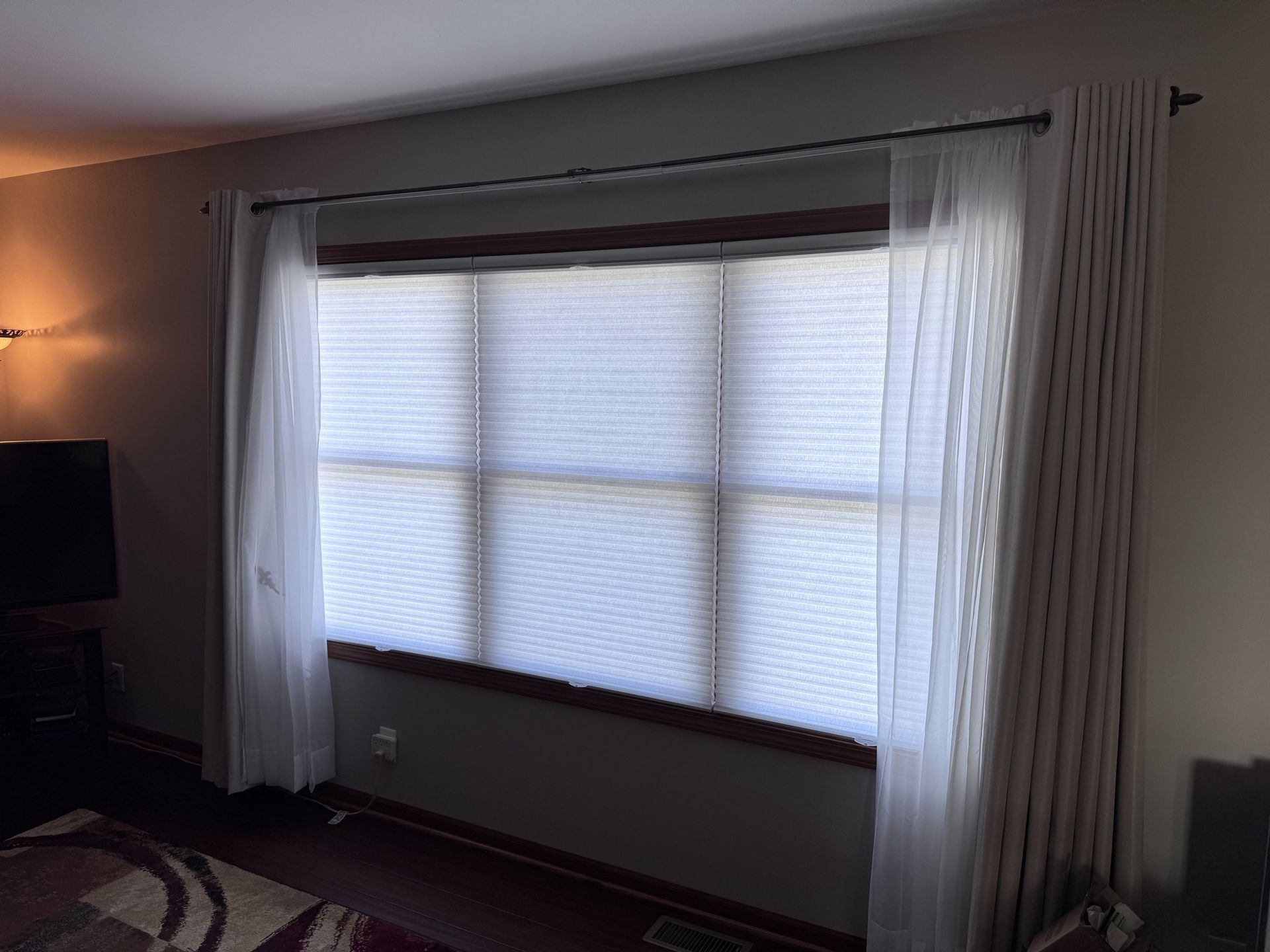 Large window with white blinds, sheer curtains, and a dark curtain rod.