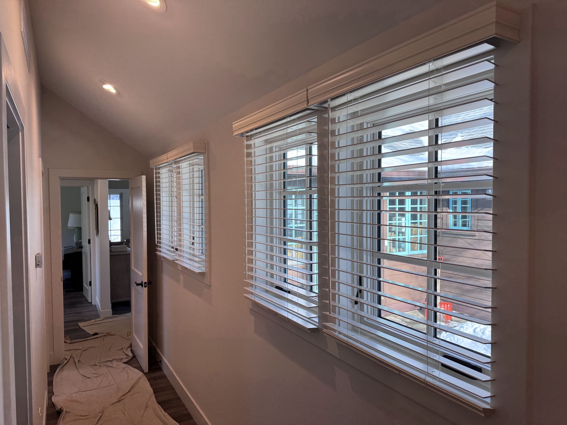 Hallway with three windows, each with white blinds and frames. Interior shot.