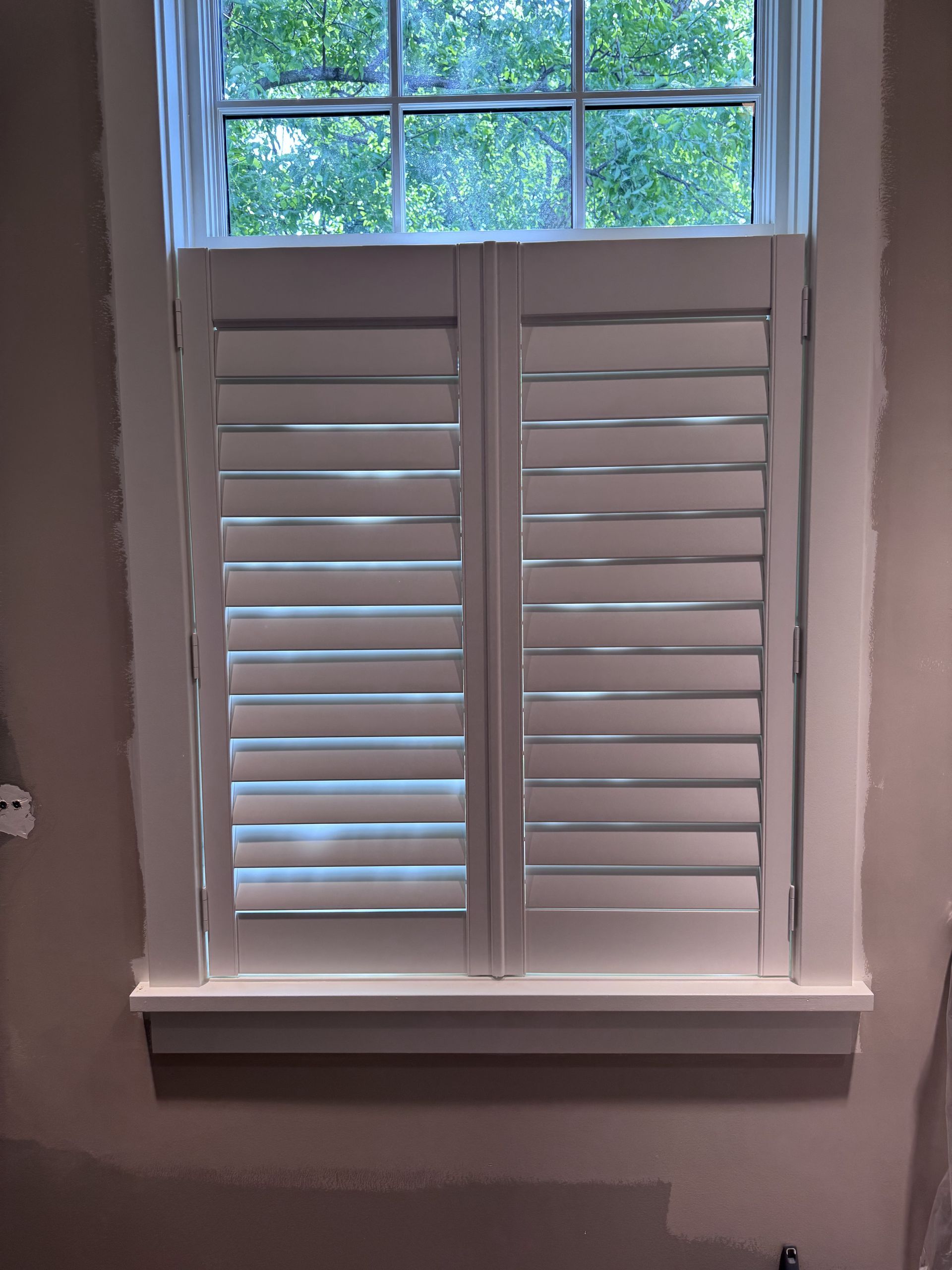 White window shutters on a window. The shutters are partially closed.