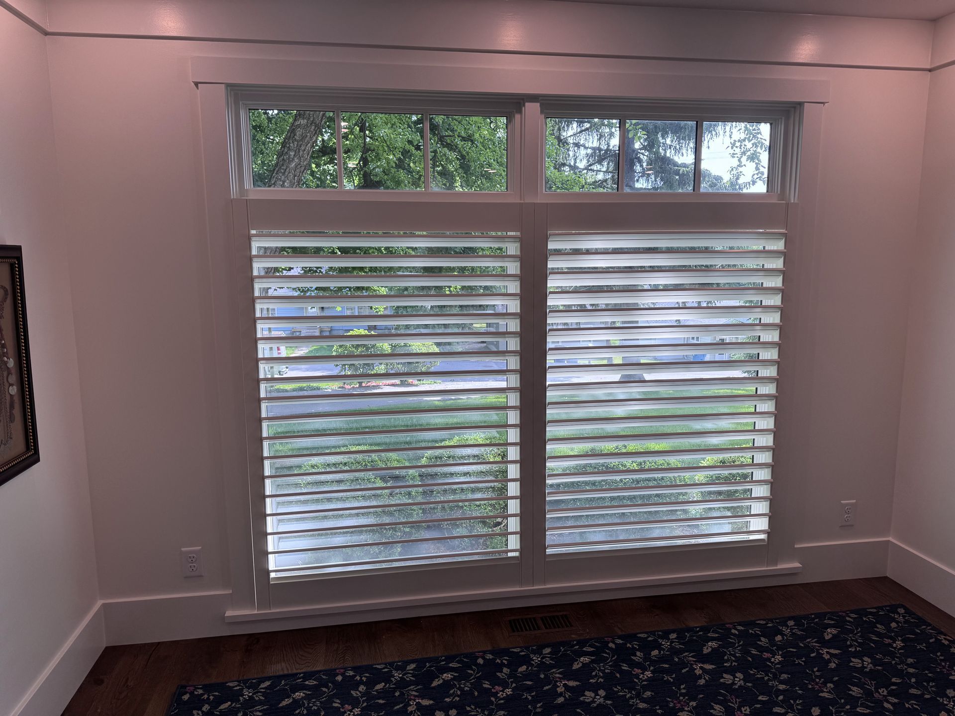 Window with white shutters, looking out onto trees. Room has white trim and dark carpet.