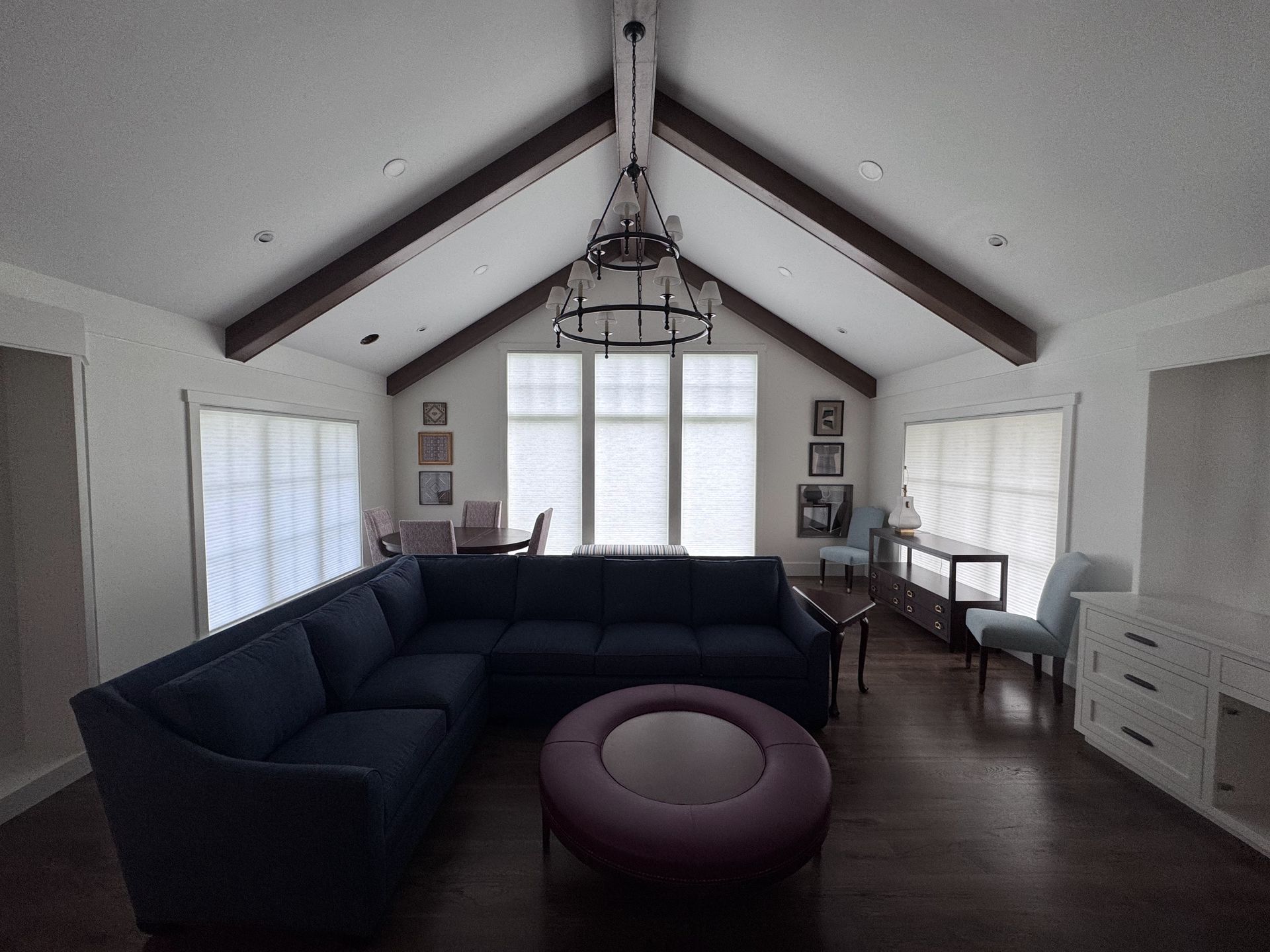 Living room with dark blue sectional sofa, purple ottoman, wood beams, and large windows.