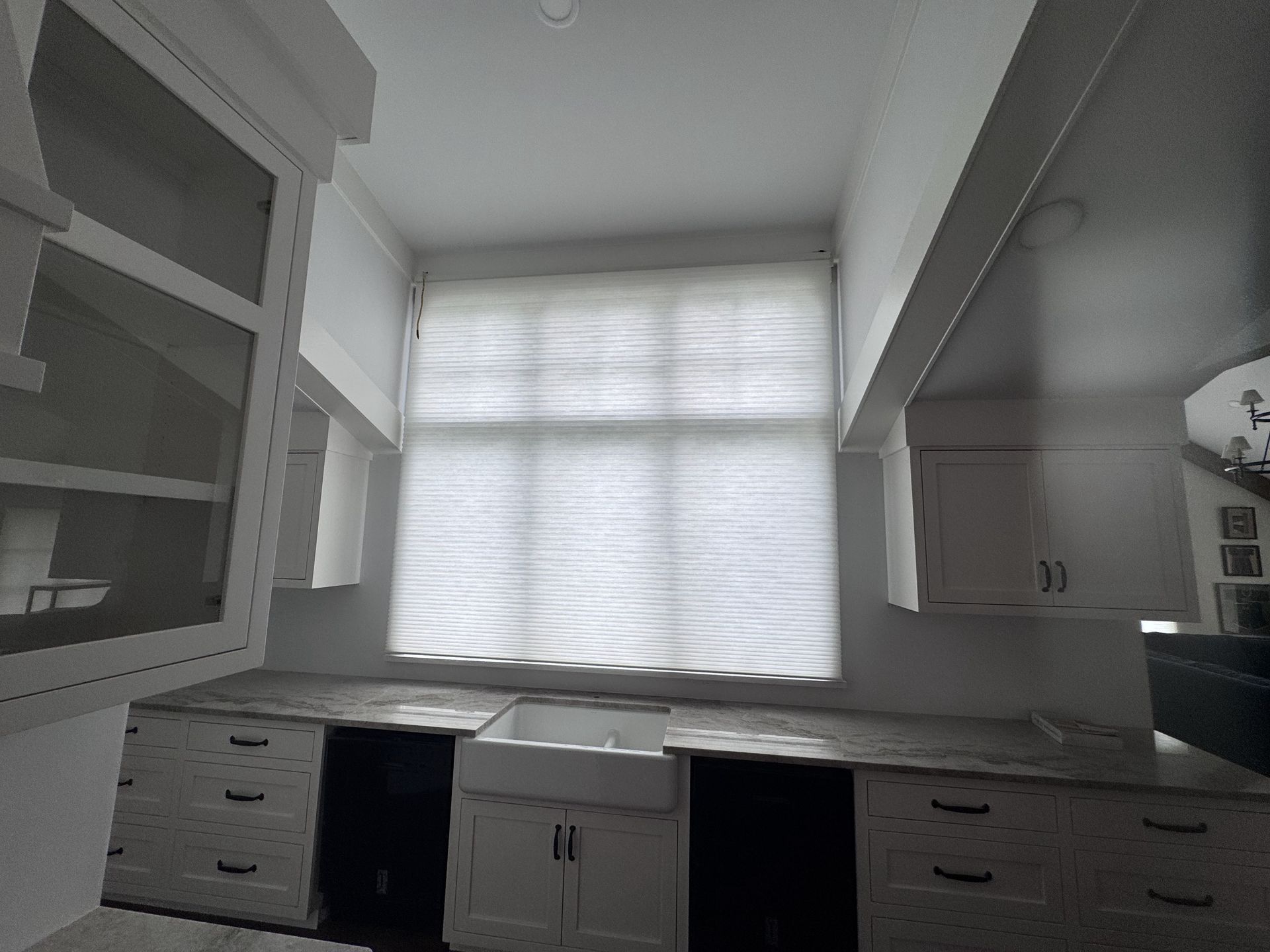 White kitchen with cabinets, sink, and window with a light-colored shade.