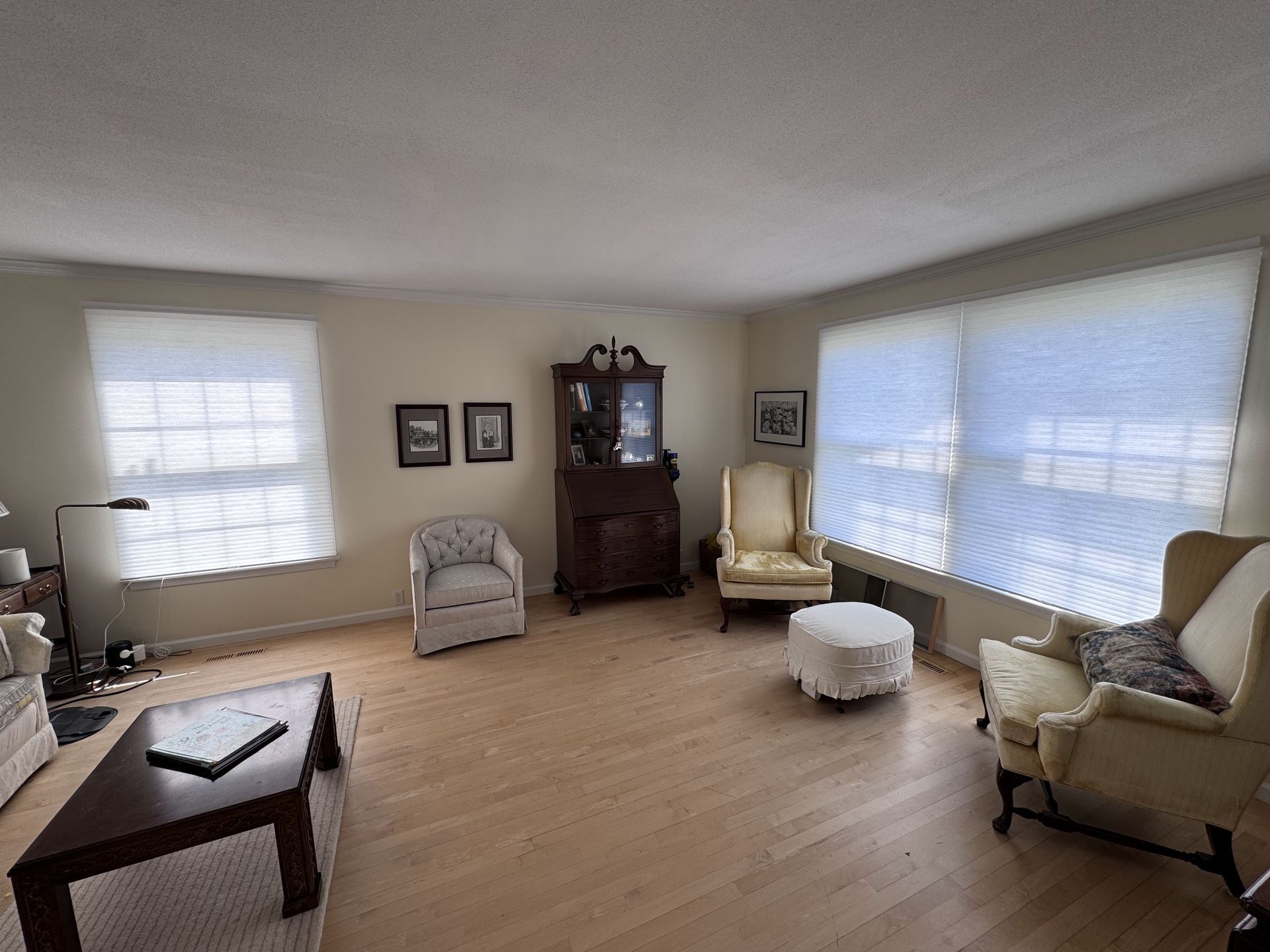 Living room with light wooden floors, chairs, windows, and a dark cabinet.
