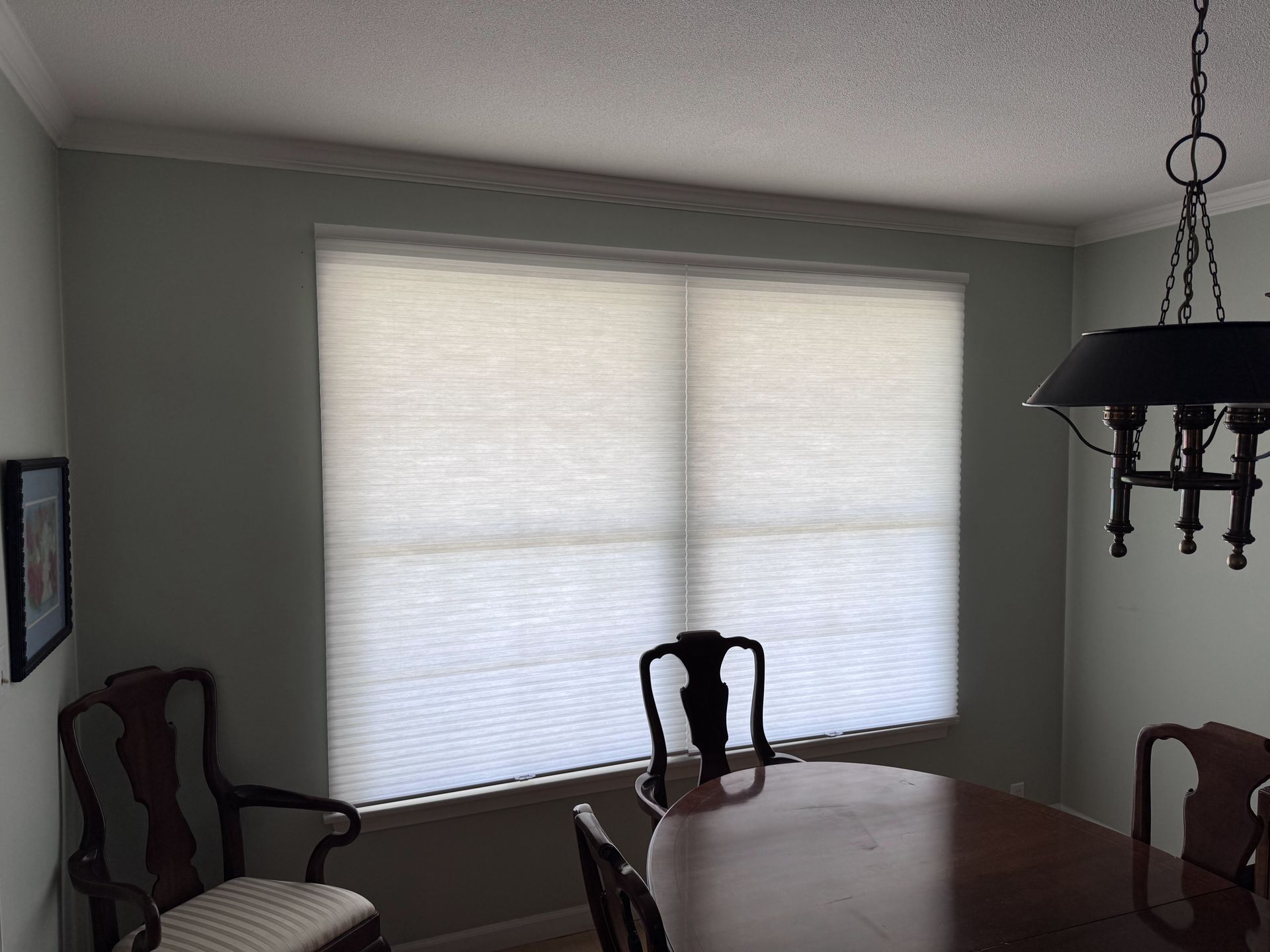 Dining room with a round table, chairs, window with blinds, and a chandelier.