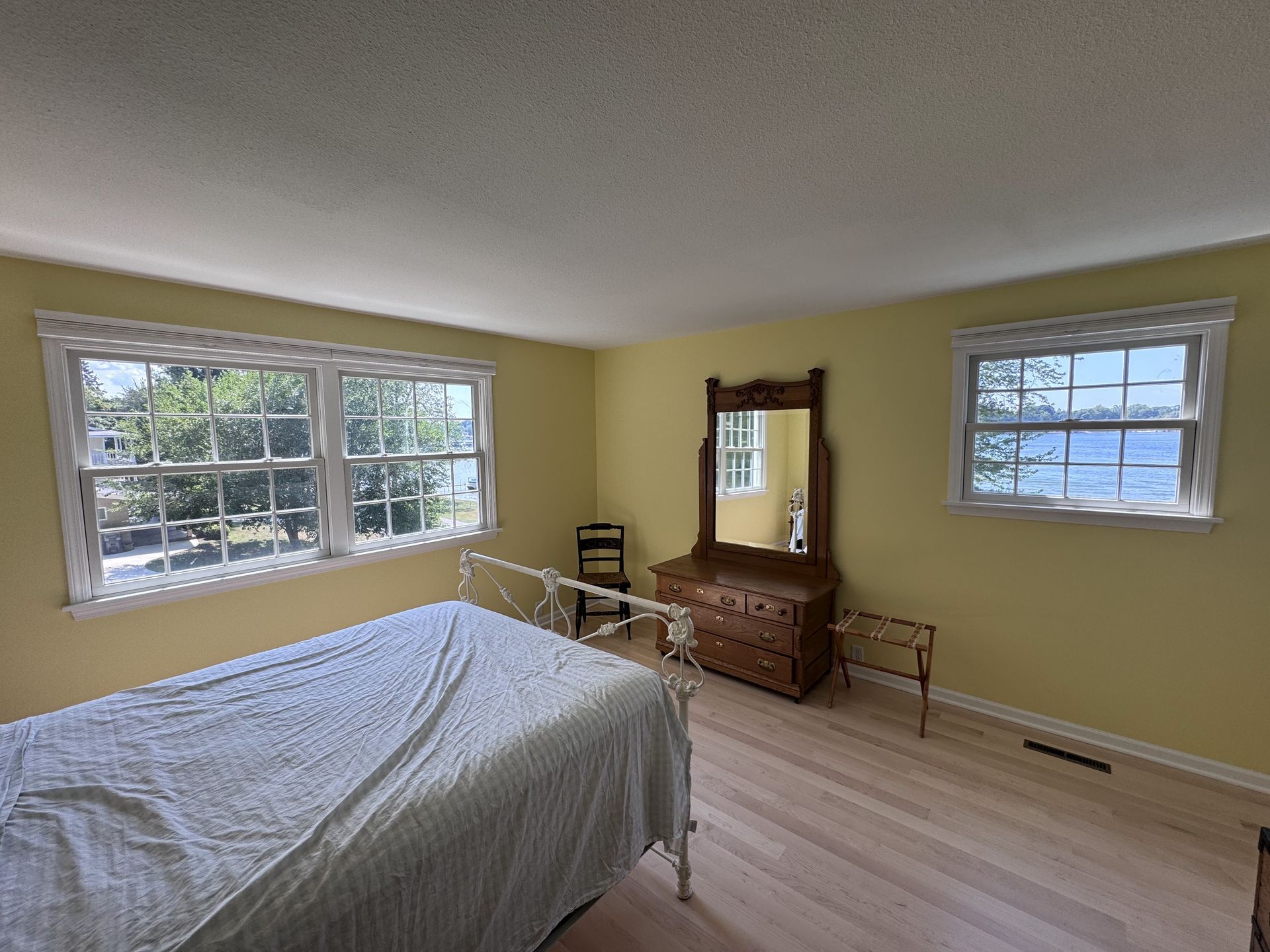 Bedroom with a white bed, dresser, and two windows, yellow walls.