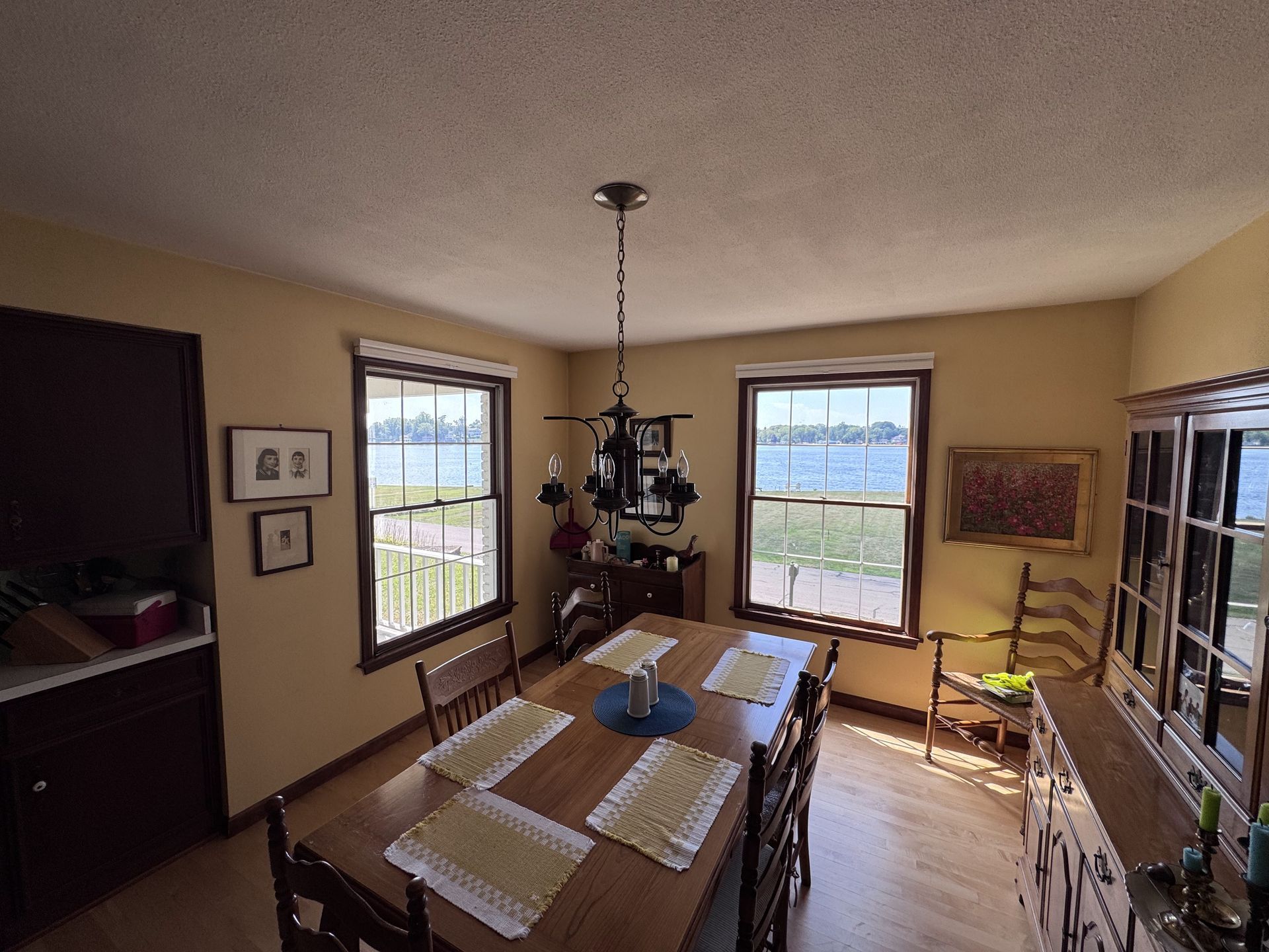 Dining room with a water view, featuring a table set for six, windows, and a dark cabinet.