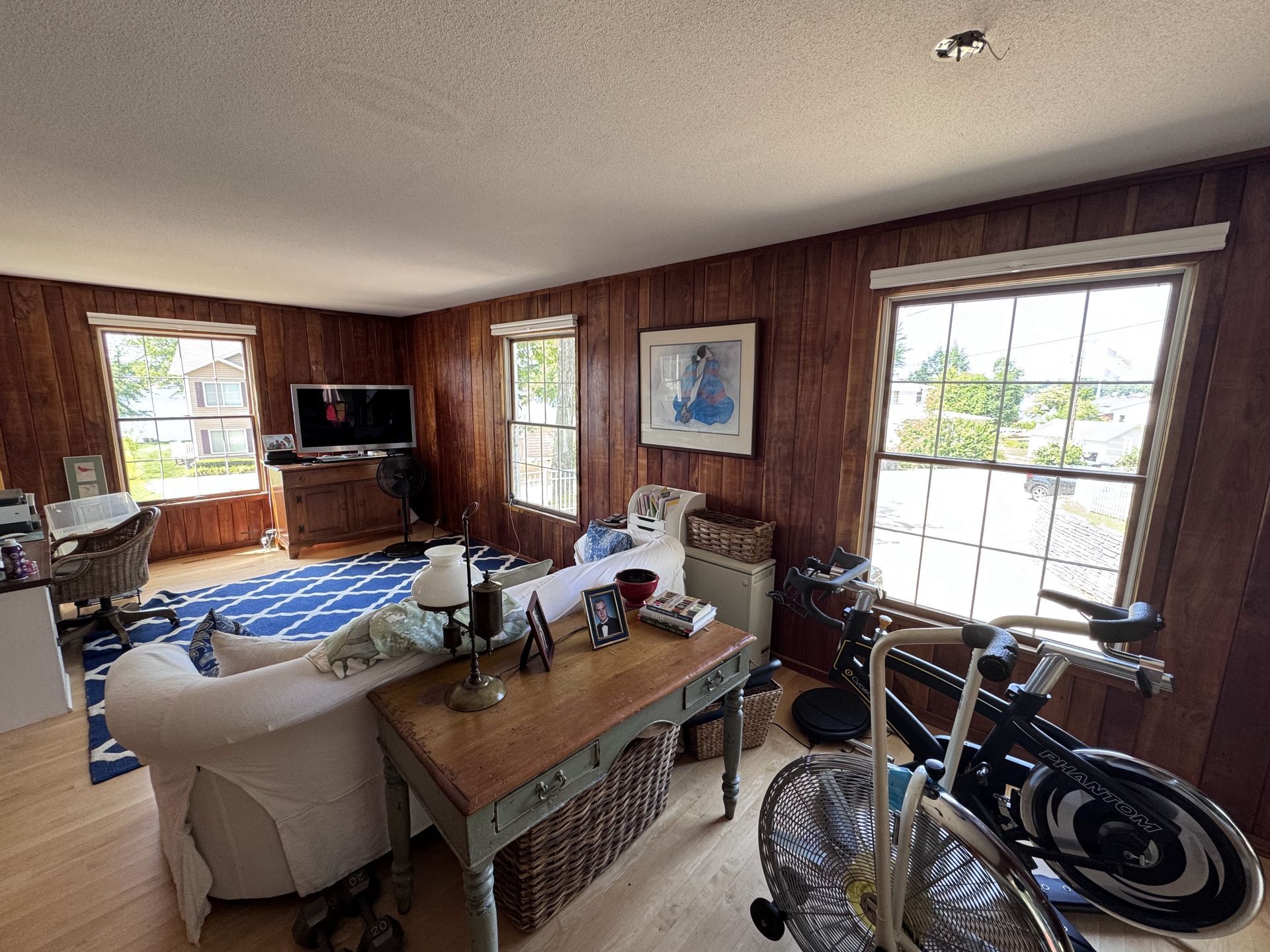 Living room with wood paneling, windows, sofa, desk, bicycle.