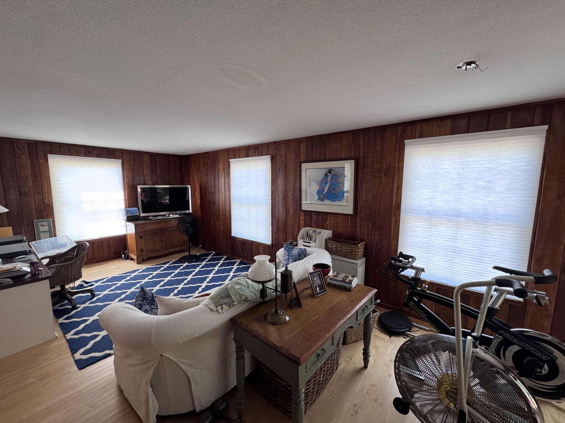 Living room with wooden paneling, windows, furniture, and an exercise bike.