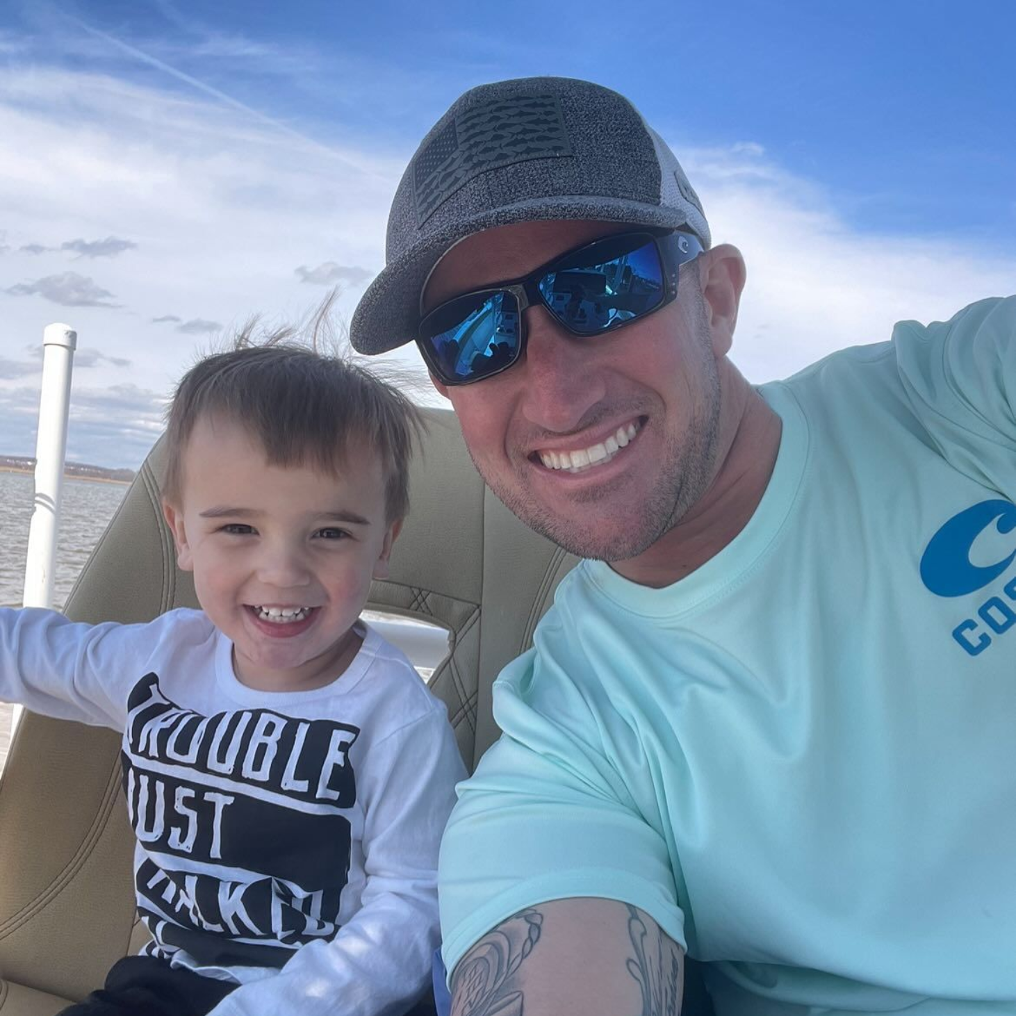 Man and child smiling on a boat, man in sunglasses and hat, child wearing a 