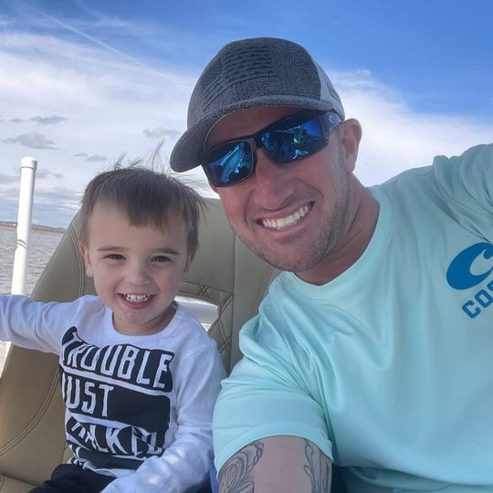Man and child smiling on a boat, the sky is blue.
