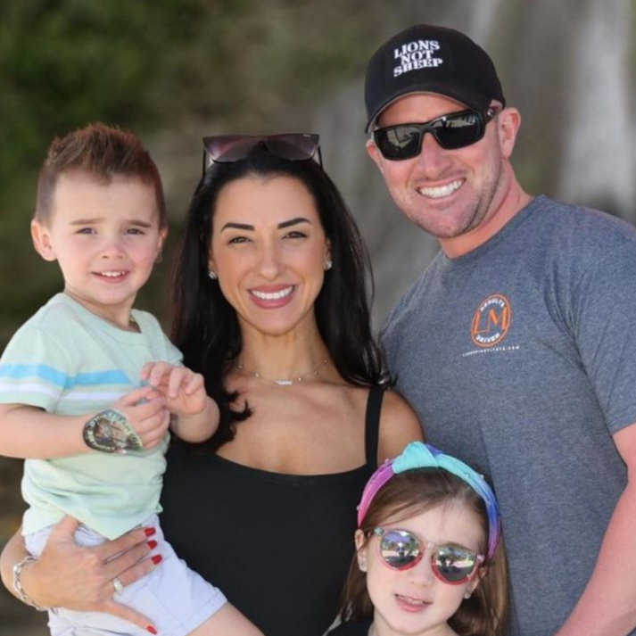 Family of four smiles for a photo; two children, a woman, and a man pose in front of a waterfall.