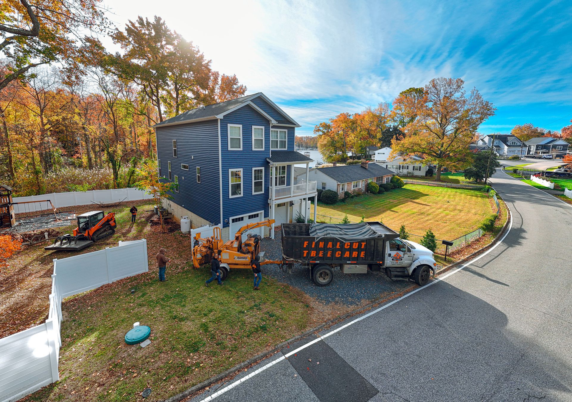 An arborist in a bright orange safety vest suspended in a tall evergreen tree, performing tree pruning.