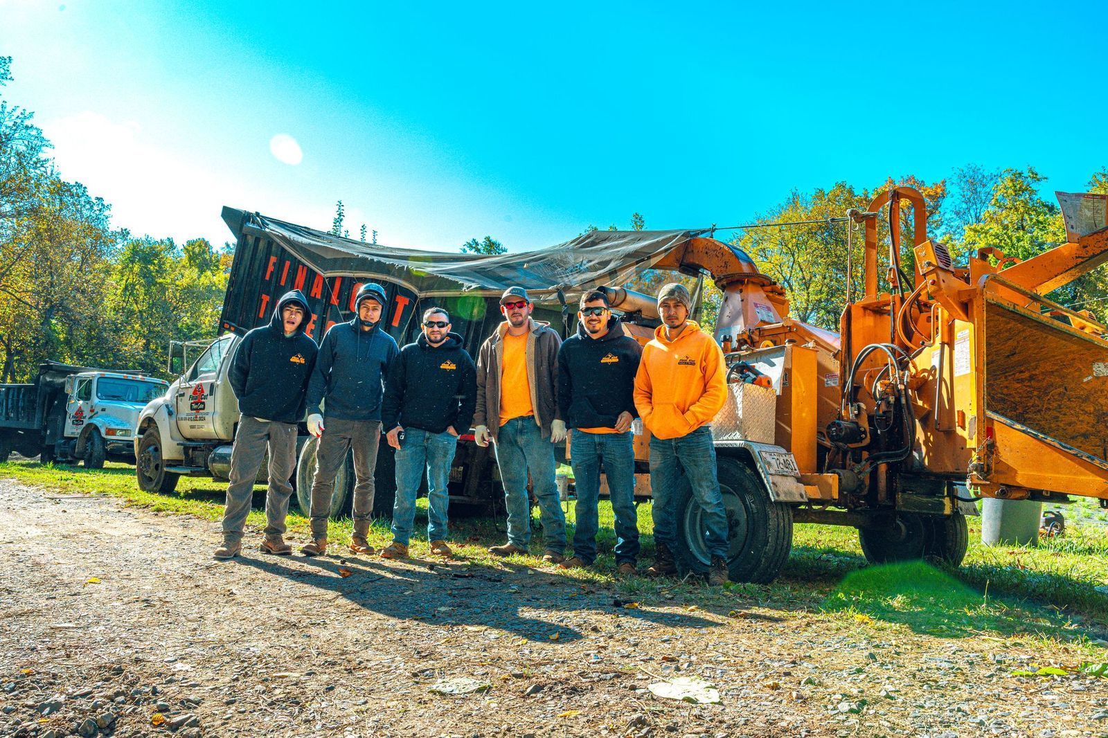 Group of people posing with wood chipper outdoors.