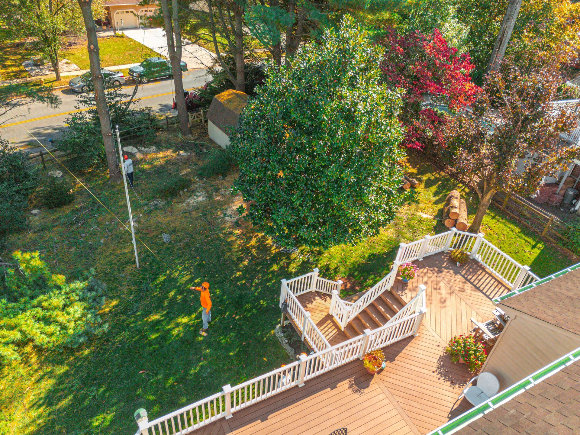 Overhead view of a deck and yard with a person, tree, and surrounding houses in daylight.