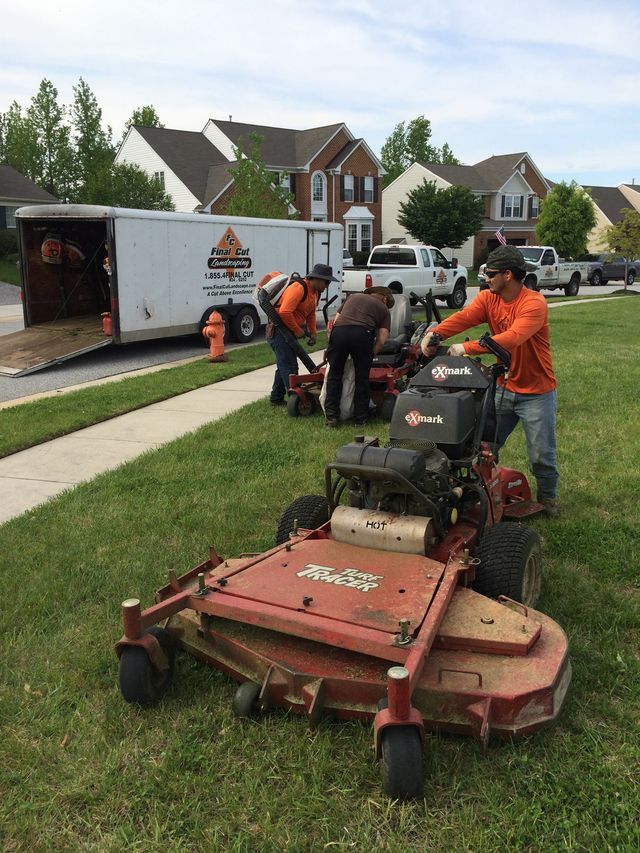 Lawn care crew with trailer, mower, and equipment, on residential lawn. Workers in orange shirts.